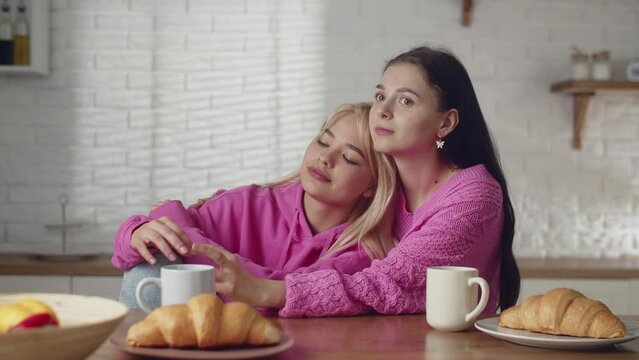 A young lesbians couple spending time together at home. Holiday with girlfriend. Cute couple lesbians drink coffee with french croissant. Stroking head of partner, idyllic relations