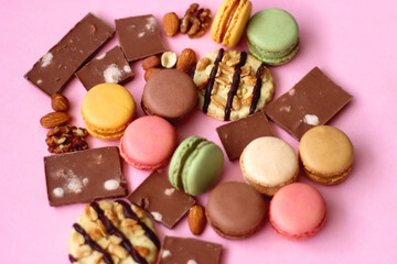 Pastel macarons, almond chocolate, peanut butter cookies and various nuts on bright pink background. Selective focus.