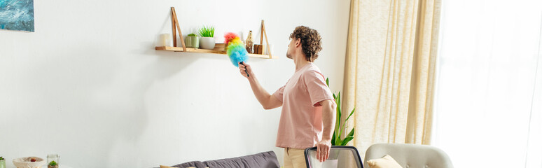 Man in living room, holding a duster.