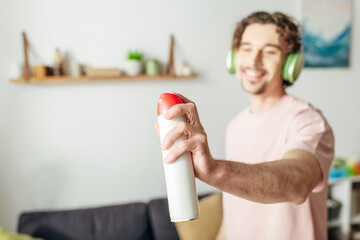 A man in cozy homewear holds a spray while wearing headphones, engrossed in musical harmony.