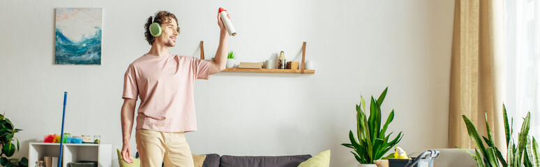 A man in cozy homewear holds a spray in a living room.