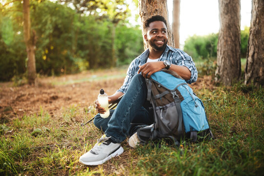Young hiker drinking energy drink while enjoys resting in nature.	