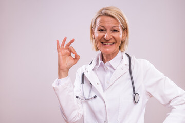 Portrait of mature female doctor showing ok sign on gray background.