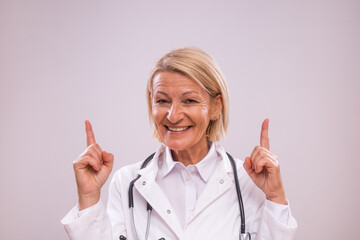 Portrait of mature female doctor pointing on gray background.