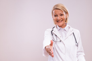 Portrait of mature female doctor  showing  handshake gesture on gray background.