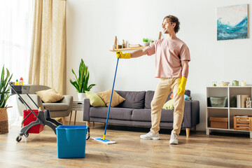 A handsome man in cozy homewear cleaning the living room with a mop and bucket.