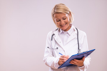 Portrait of mature female doctor  writing notes  on gray background.