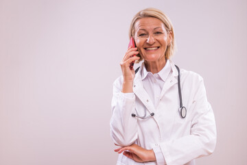 Portrait of mature female doctor using mobile phone  on gray background.