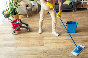 A handsome man in cozy homewear cleans the floor with a mop.