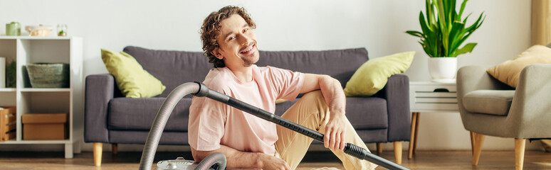 A man in cozy homewear sits on the floor with a vacuum.