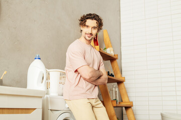 A handsome man in cozy homewear standing next to a washing machine, ready for laundry day.