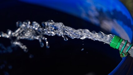  A stream of clear water from a hose into a barrel as an abstract background.                      ...