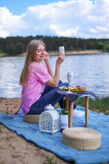women with glass of wine or limonade making picnic outside. Positive model sitting close to lake,...