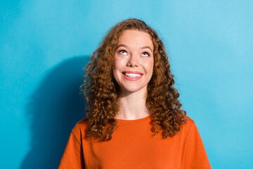 Photo portrait of youth beautiful funny girl with wavy hairstyle wearing orange t shirt looking above head isolated on blue color background