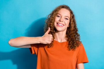Portrait photo of youngster cheerful girl with beautiful curly red hair wearing orange t shirt showing like symbol isolated on blue color background