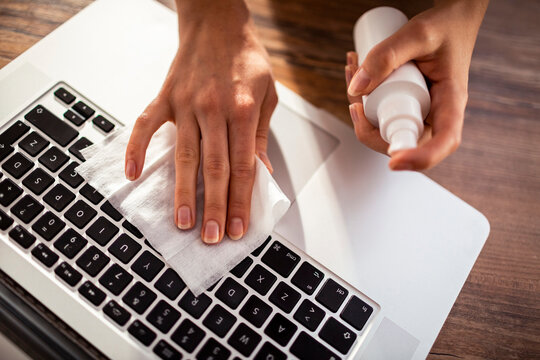 Woman disinfecting laptop keyboard with cleaning wipe