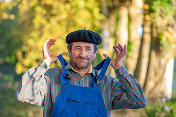 Portrait of a Frenchman, wearing a beret and blue dungarees smiling and gesticulating to camera