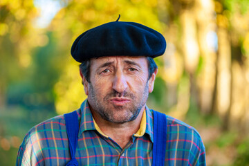 Portrait of a Frenchman, wearing a beret and blue dungarees smiling and gesticulating to camera