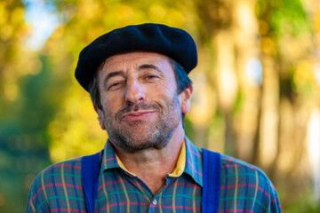 Portrait of a Frenchman, wearing a beret and blue dungarees smiling and gesticulating to camera