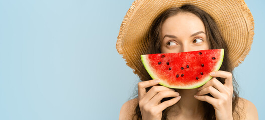 portrait of a happy woman with a slice of watermelon, looking slyly to the side on a blue background