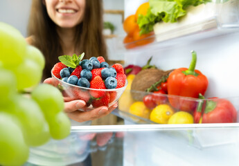 happy woman taking out a plate of berries from the refrigerator