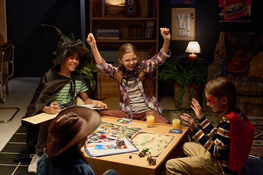 Two ecstatic kids in costumes of their characters raising hands and expressing triumph of victory in tabletop game with friends