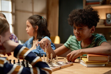 Youthful African American boy looking at checkmate sitting in front of him and holding white pawn...
