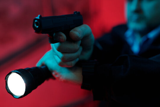 Hand of professional security guard keeping forefinger on gun trigger and lighting dark corridor with flashlight while observing place