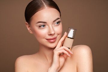 Portrait beautiful young woman with clean fresh skin. Model with foundation makeup bottle....