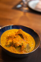 Satsivi is a traditional Georgian dish of chicken in walnut sauce in a blue plate on a table with cutlery and a glass in a restaurant. Vertical photo