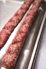 Close-up of a raw lula kebab with spices on skewers on a metal tray on the table, selective focus. Vertical photo