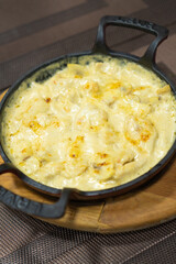 Close-up of mushrooms in sour cream sauce on a cast-iron frying pan for serving dishes in a restaurant. Vertical photo