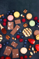 Macarons, chocolate, cookies, berries and various nuts on dark blue background. Selective focus.
