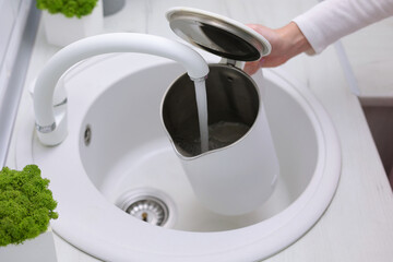 A girl pours clean water into a kettle from a kitchen tap. Purified water