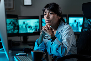 Serious young woman in uniform of security guard concentrating on observing cctv video while...