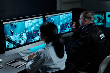 Two intercultural male and female officers in uniform sitting in front of computer monitors with...