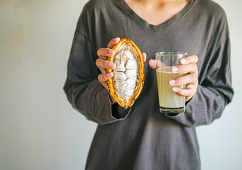 Fresh Cacao water in glass and half sliced ripe yellow cacao pod with white cocoa seed in the hands...