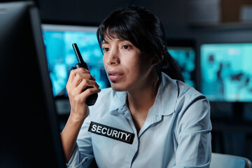 Young serious Hispanic woman in uniform of security guard sitting in front of computer screen and...