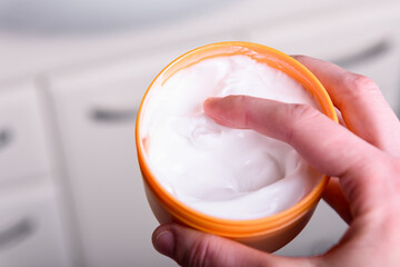 Young woman using body care cream in bathroom.