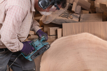 Carpenter polishing giant piece of wood using sanding machine in furniture factory