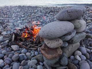 View of campfire in stone place on round pebbles beach on the background of sea and evening sky....