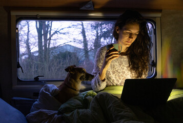 Woman in pajamas using the computer in the bed of a motorhome with her dog