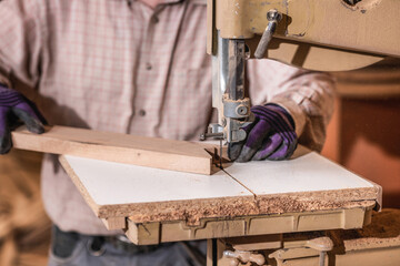 Carpenter using bandsaw, cutting wooden boards at a woodworking