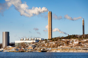 Smoke emerging from chimneys near sea against sky