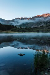 Fototapeta premium Misty Lake with Mountain Reflections at Sunrise 