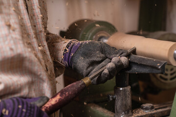 Woodworker shapes detail of a wooden chair with gouge in carpentry workshop