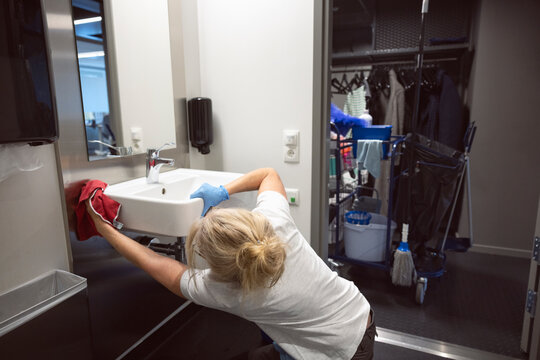 Mature female janitor cleaning sink in bathroom