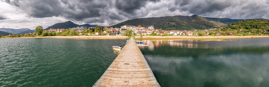 In Plav, Montenegro, tourists enjoy the tranquil beauty of the lake from the pier, with breathtaking mountain views and clear reflections in the water.