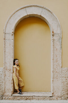 M&auml;dchen im gelbwei&szlig; gestreifen Jumpsuit steht posiert in einem gelben Mauervorsprung