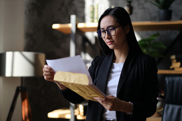A confident Korean businesswoman in a corporate office, examining financial reports with...